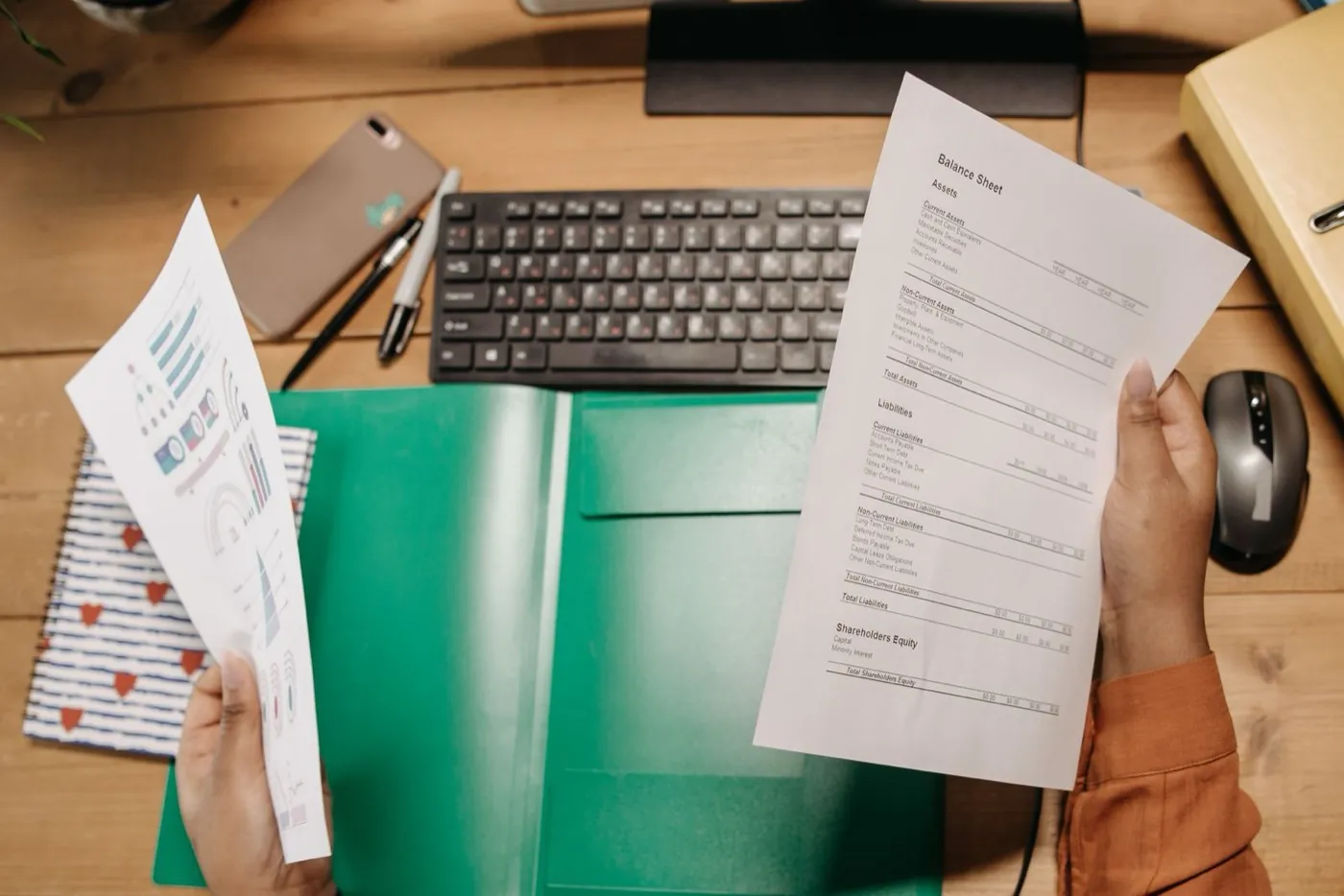 Hands holding printed financial statements over an office desk